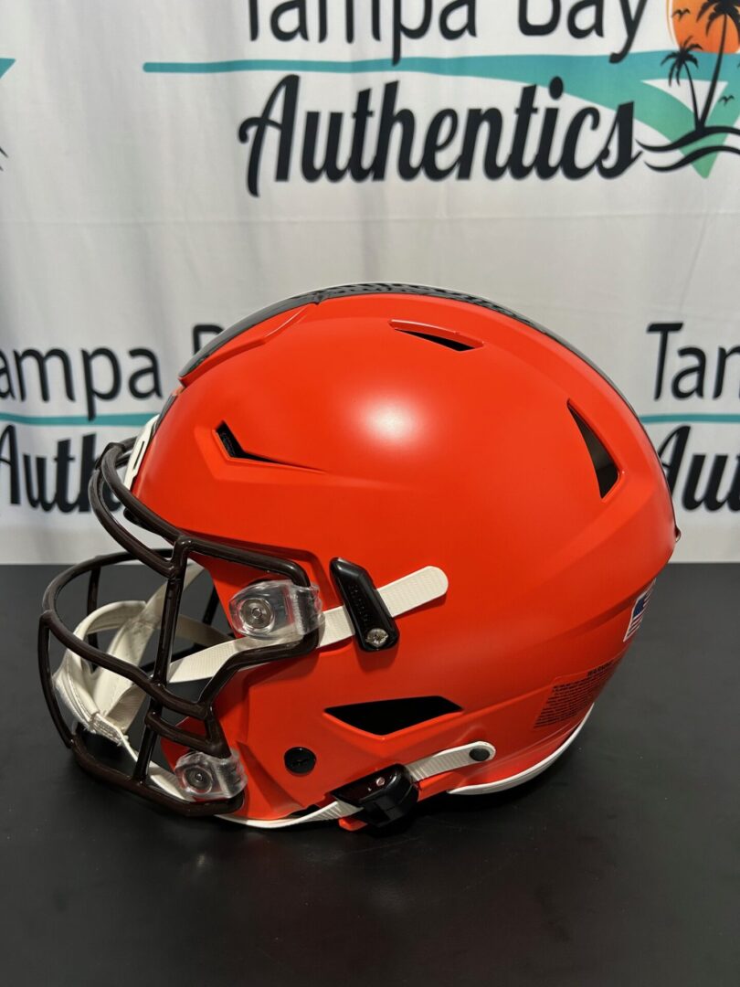 Bright orange football helmet with a black faceguard on a black surface.