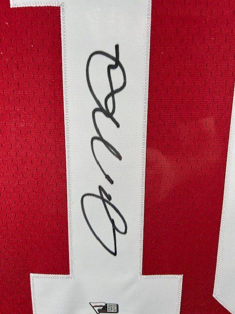 A black signature on a white paper strip against a red background.