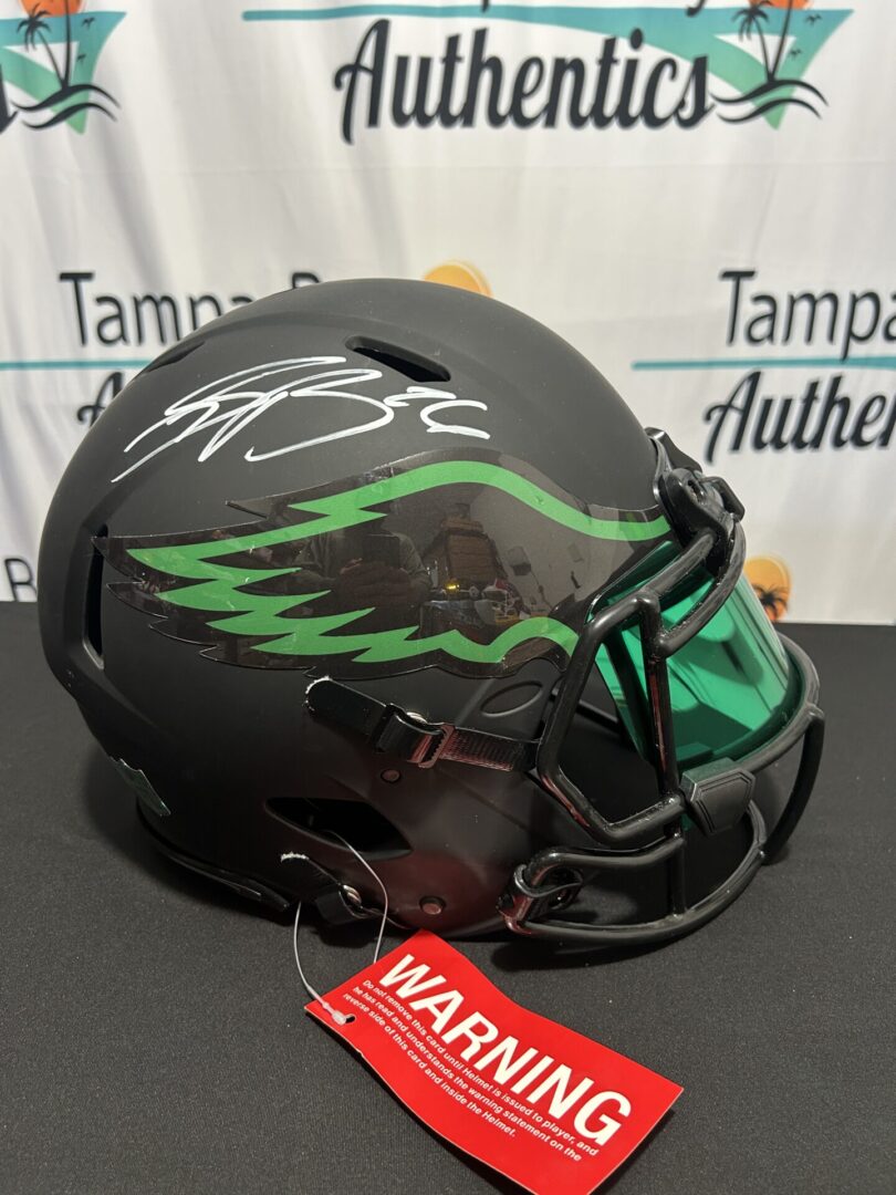 Black football helmet with green visor, autograph.